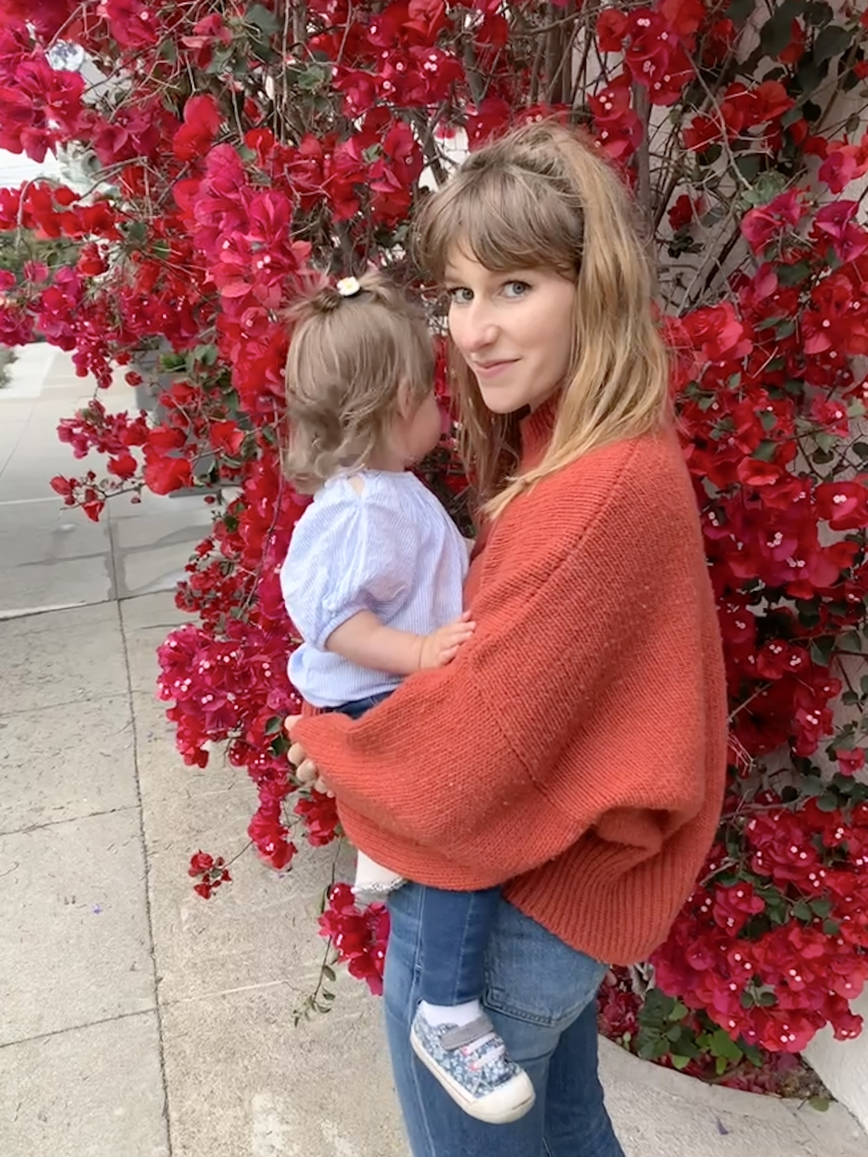 a person holding a child in front of a tree with red flowers