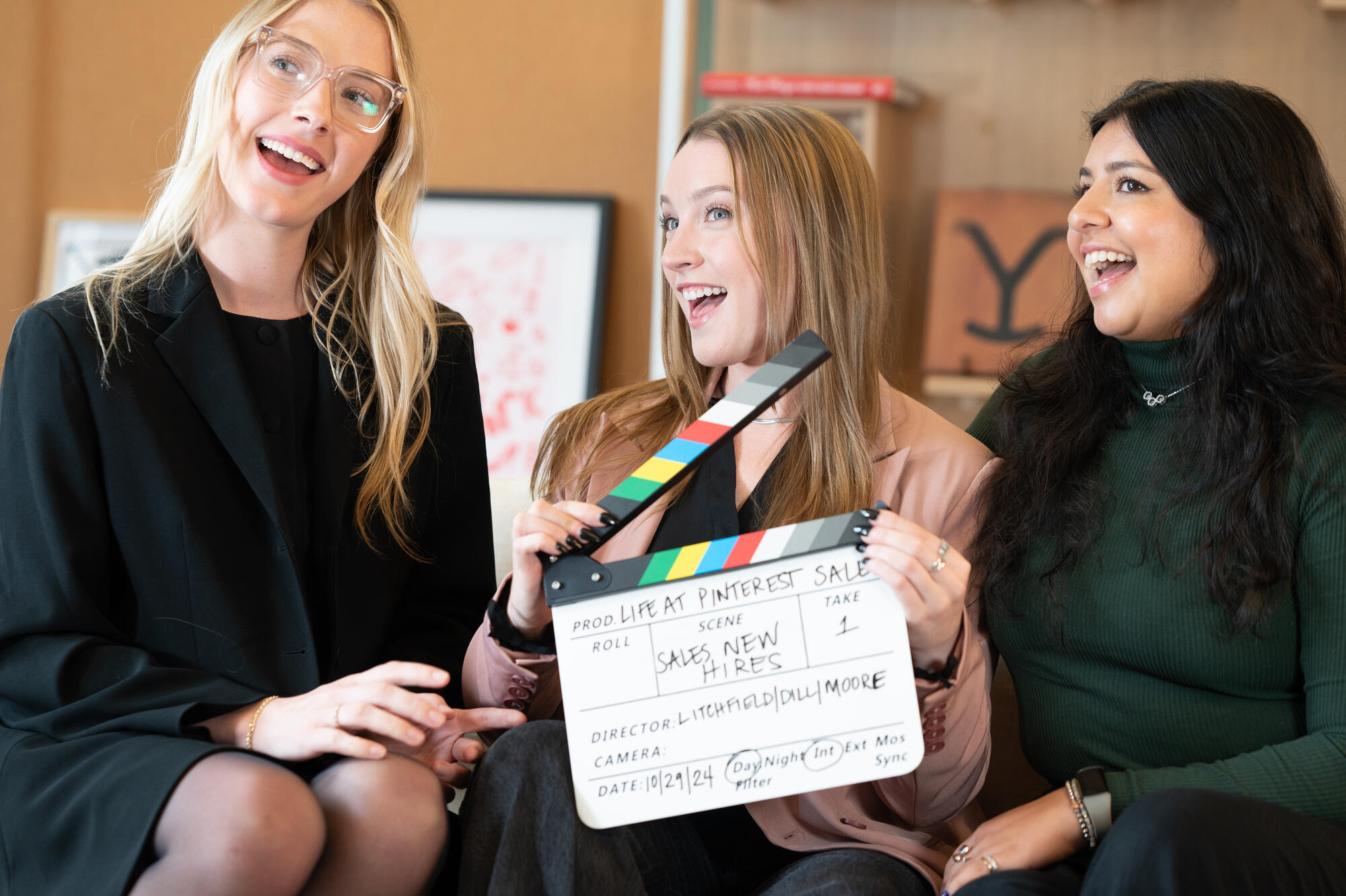 a group of women sitting on a couch holding a clapper board